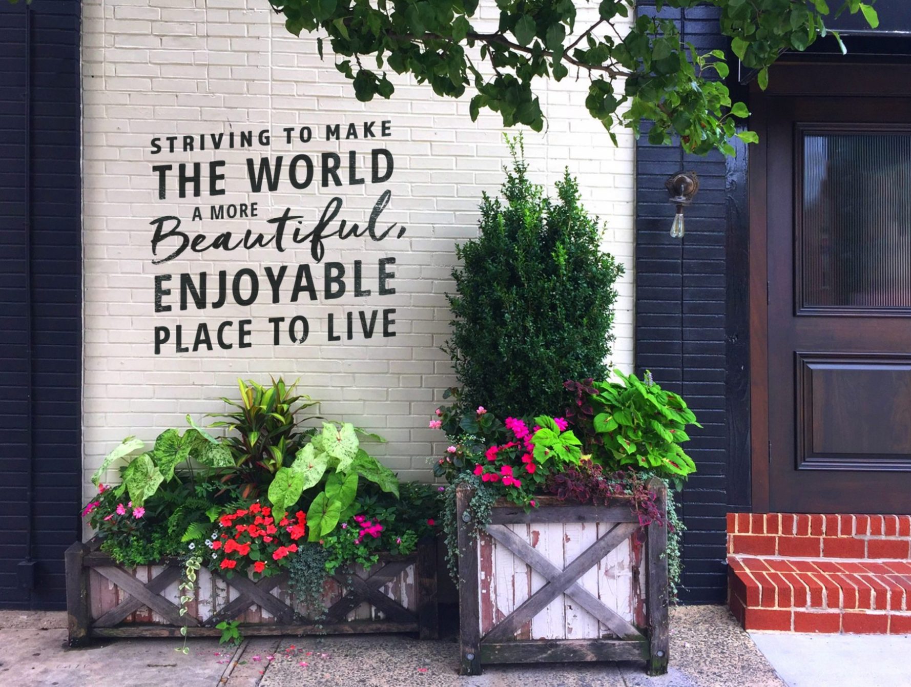 Colorful Summer Planters in front of a wall that says "Striving to Make The World A More Beautiful, Enjoyable Place To Live"